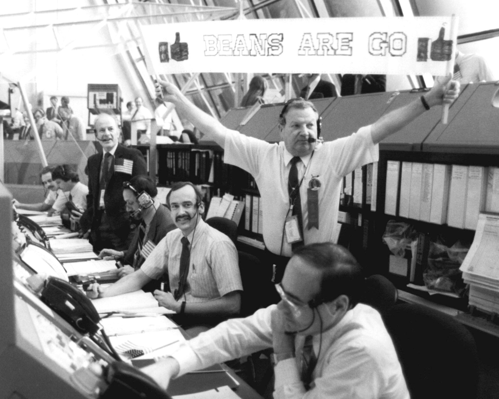 Former NASA Test Director Norm Carlson holds a "Beans are Go" sign in the Launch Control Center.