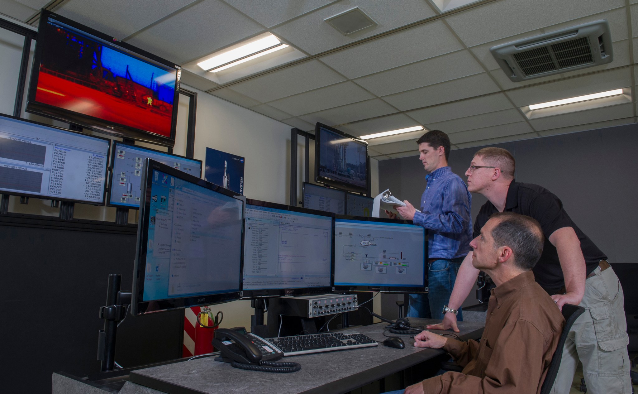 Three people looking at several computer monitors.