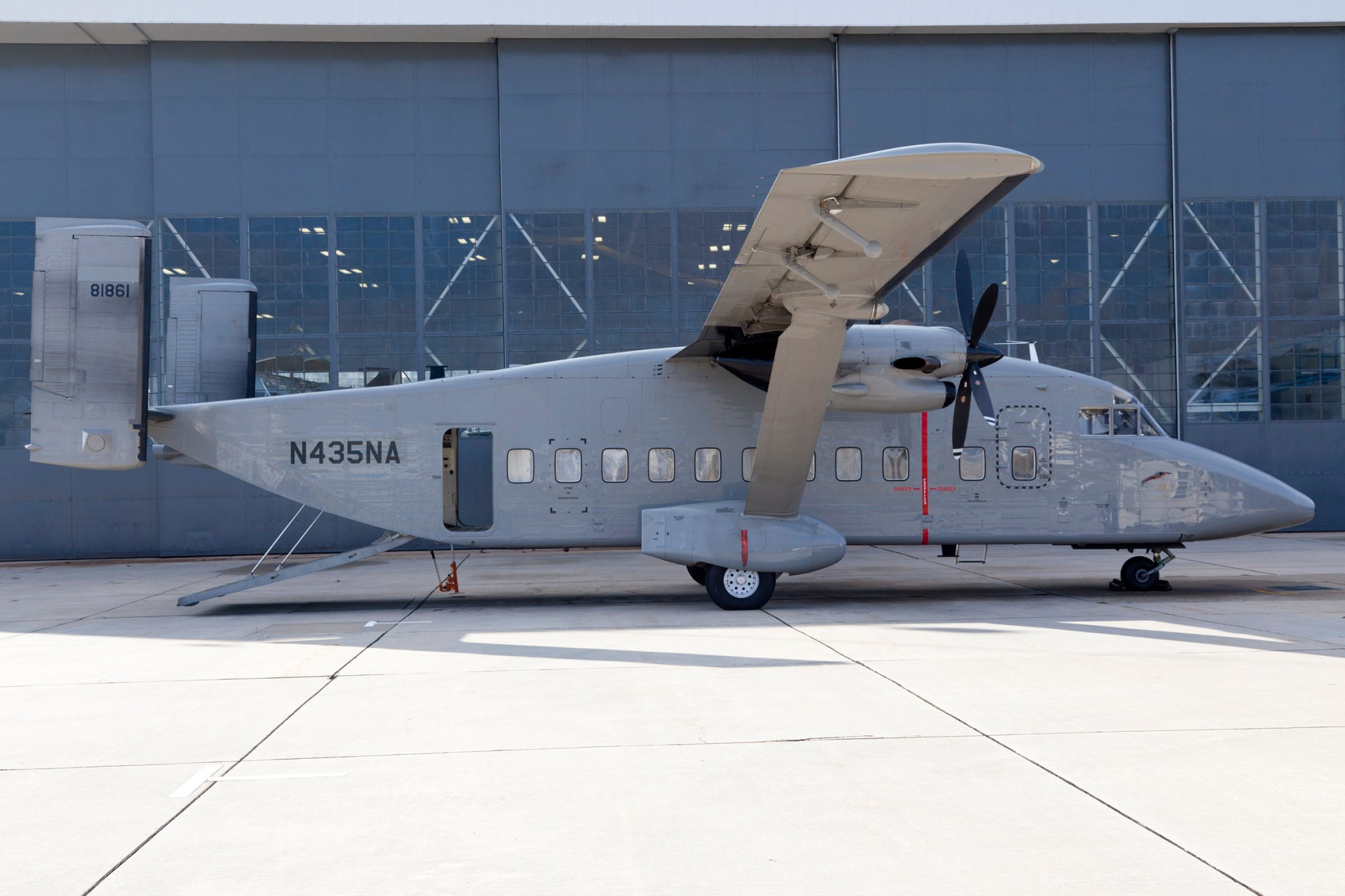 small grey plane, C23 Sherpa, in front of a hangar, there are 11 windows on the side of the plane. The numbers and letters on the back are N435NA.