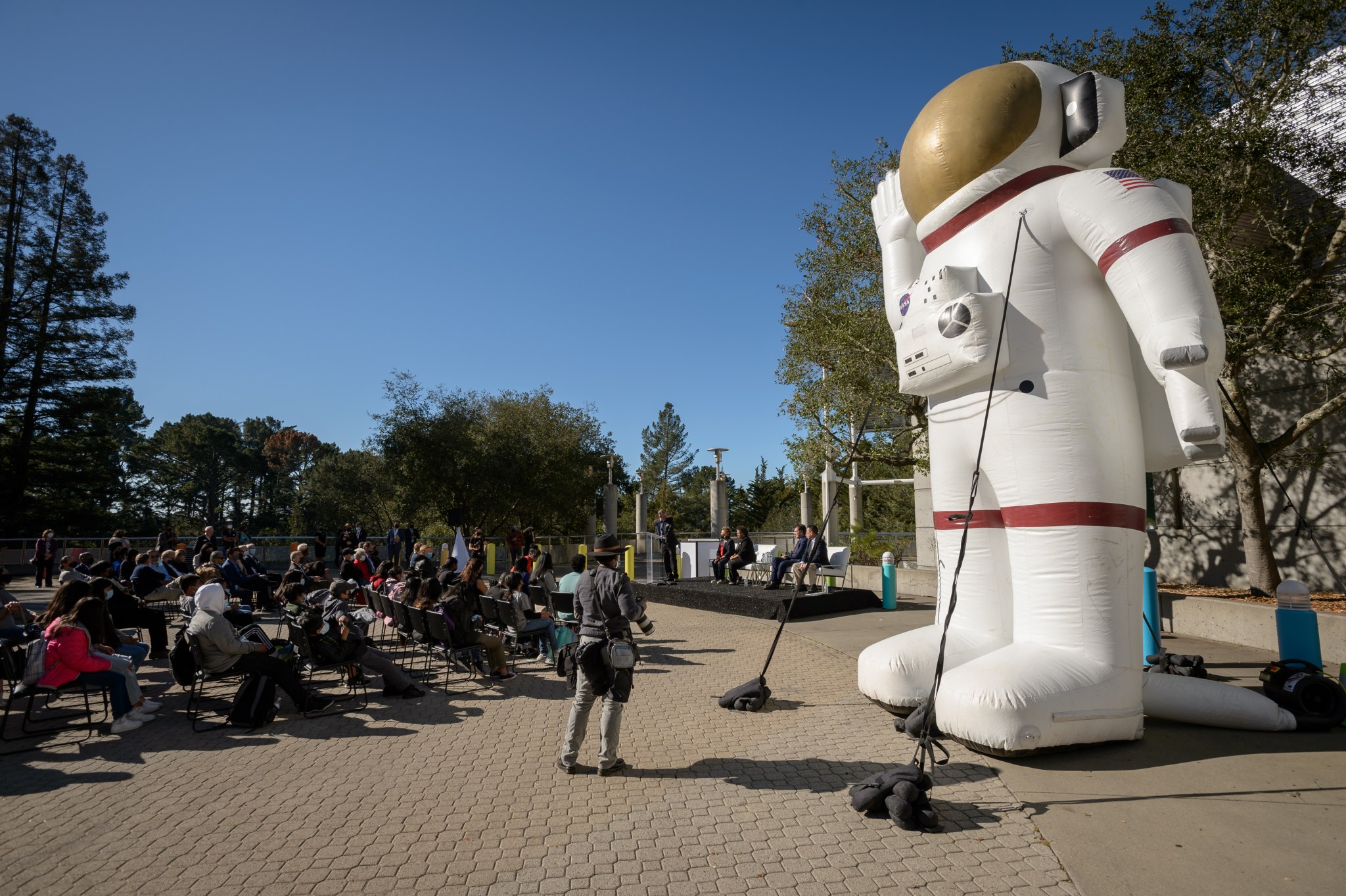 In this view, a giant inflatable model of a spacesuit stands to the right of the audience during an outdoor event at the Chabot Space and Science Center.