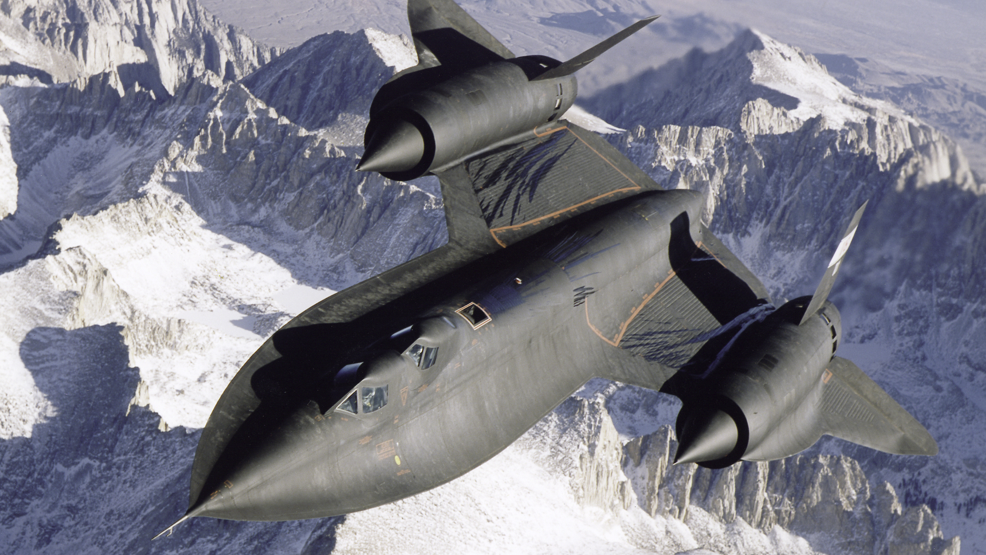 Dryden's SR-71B Blackbird in flight over snow-covered mountains.