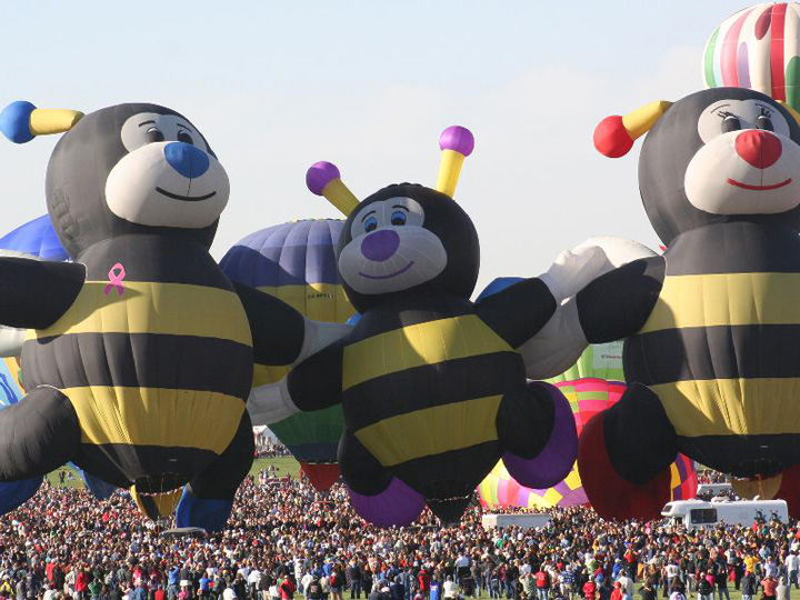 Throngs of spectators swarm the field as the Bee Family special-shape hot-air balloons.