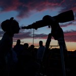 A person looking through a telescope at dusk