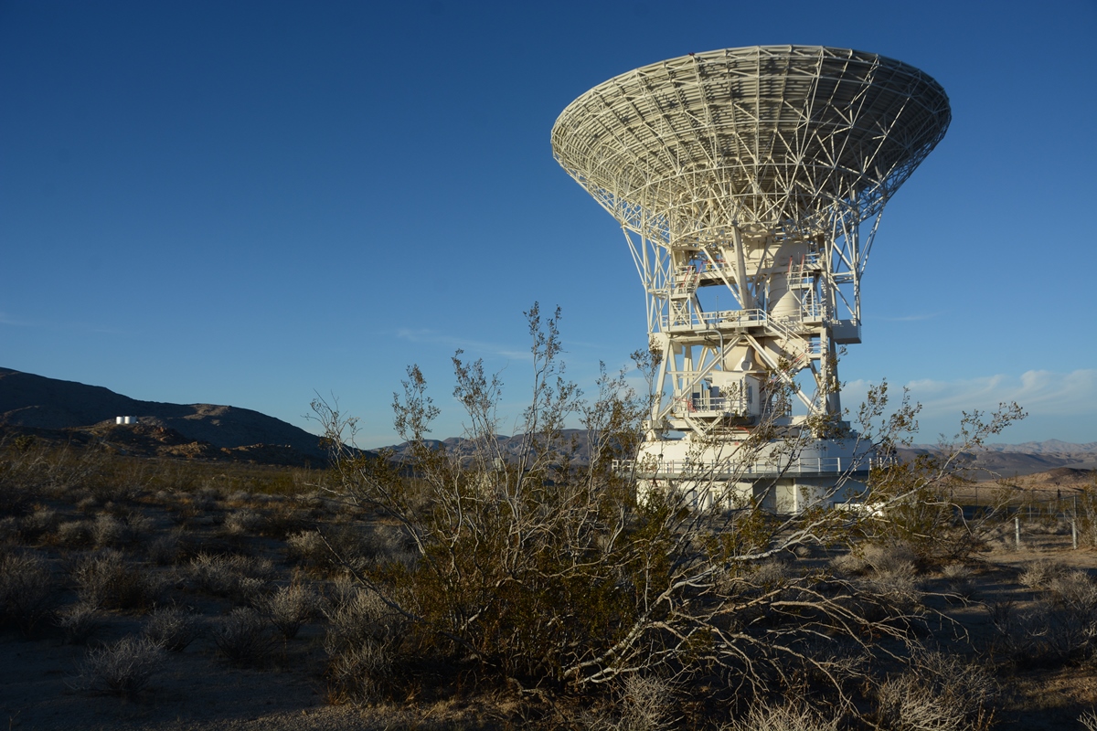 The Goldstone Apple Valley Radio Telescope points up to a bright blue sky.
