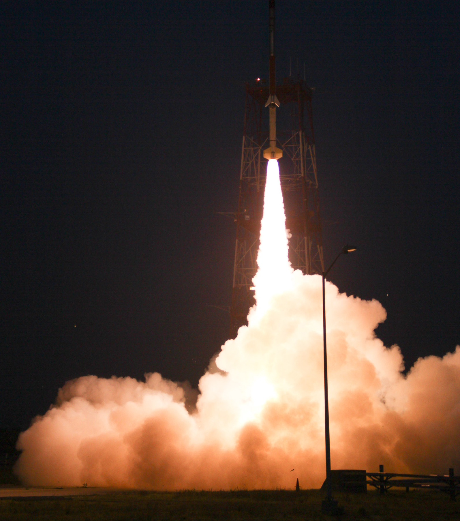 A sounding rocket launching at night with a bright white plume underneath. 