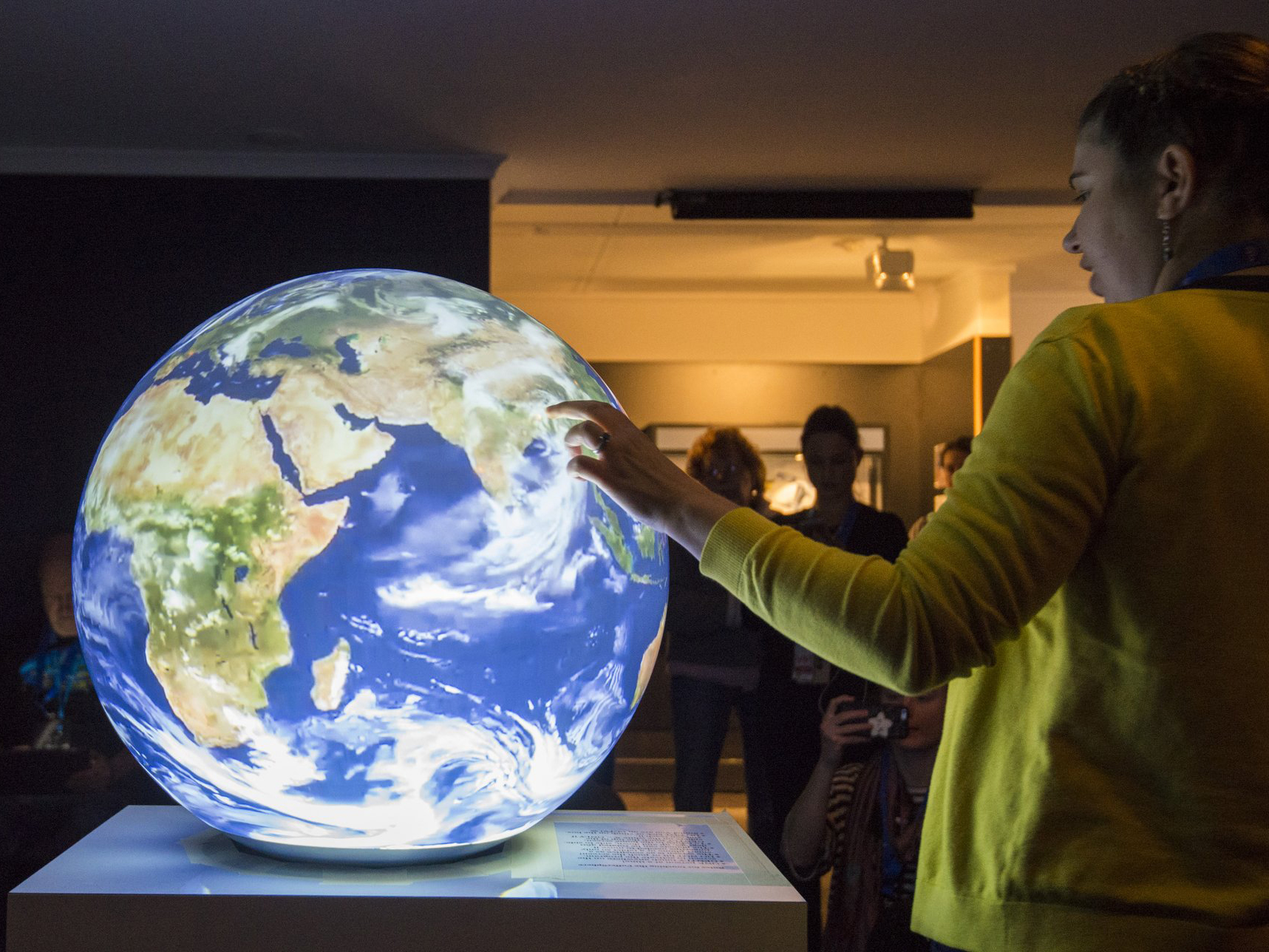 A person points at the PufferSphere, a 360-degree multi-touch, interactive display. The PufferSphere shows a view of Earth.