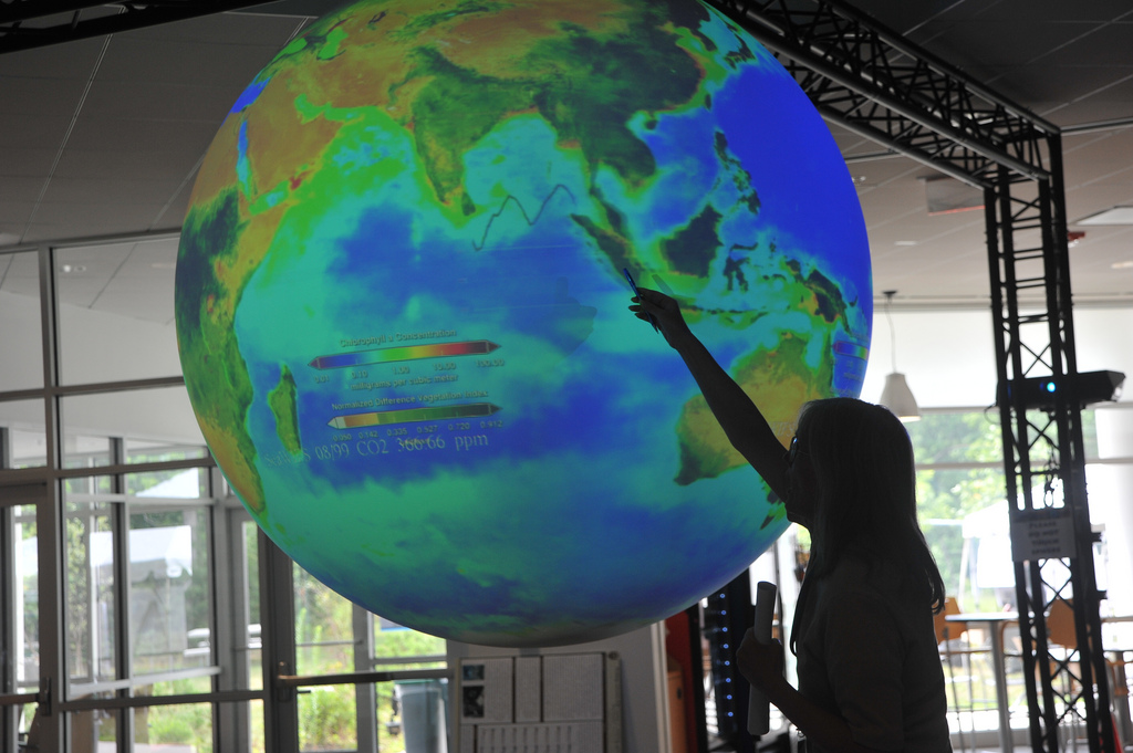 A figure points at a large Science on a Sphere exhibit displaying Earth.