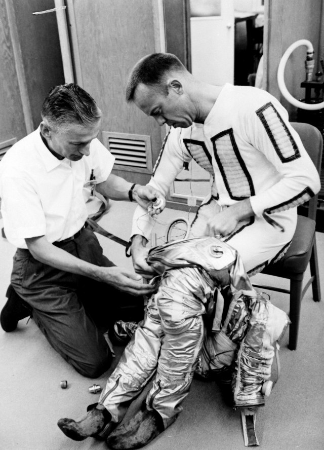 Alan Shepard sits on a chair as he is helped to get suited up for his space flight