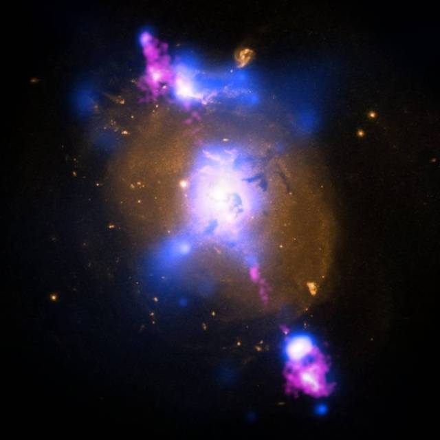 This composite image of a galaxy illustrates how the intense gravity of a supermassive black hole can be tapped to generate immense power. The image contains X-ray data from NASA’s Chandra X-ray Observatory (blue), optical light obtained with the Hubble Space Telescope (gold) and radio waves from the NSF’s Very Large Array (pink).