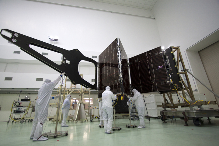 Workers wearing white suits work on a piece of the Juno spacecraft