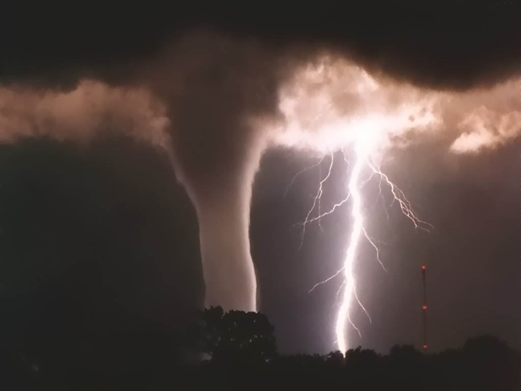 Funnel cloud of a tornado and a giant sky-to-ground lightning bolt against a night sky