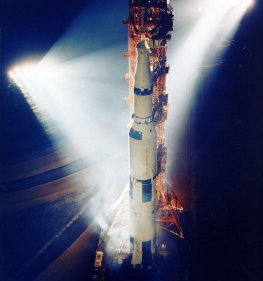 Saturn V rocket on the launch pad, illuminated by lights at night