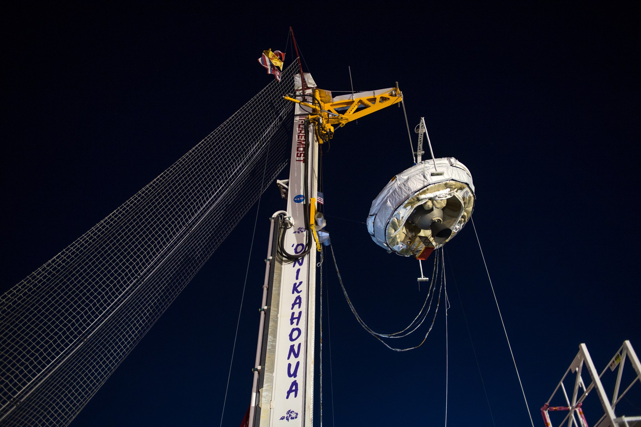 Saucer-shaped supersonic decelerator suspended from rig against night sky