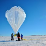 Three people hold onto a large balloon against the Antarctic landscape