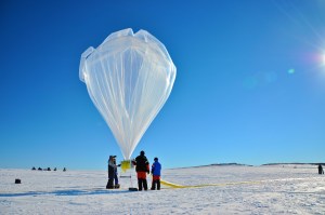 Three people hold onto a large balloon against the Antarctic landscape