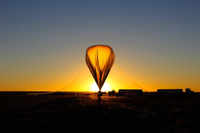 A scientific balloon is partially inflated in the shape of a teardrop in front of a bright orange sunset.