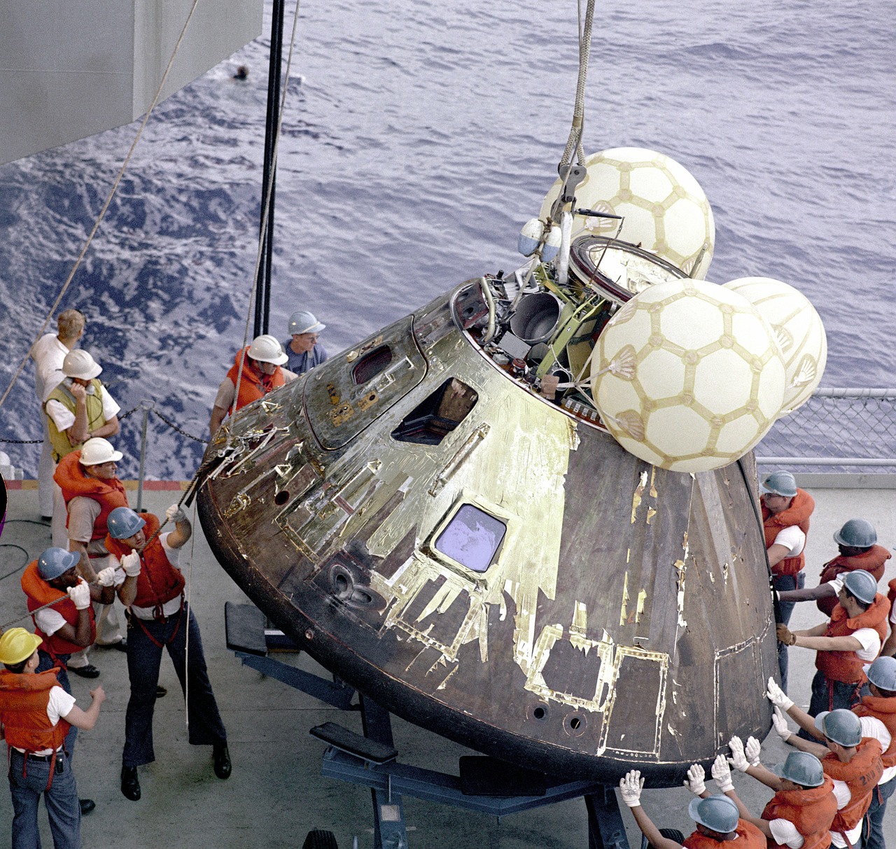 Ship's crew moving an Apollo capsule out of the water to the ship's deck