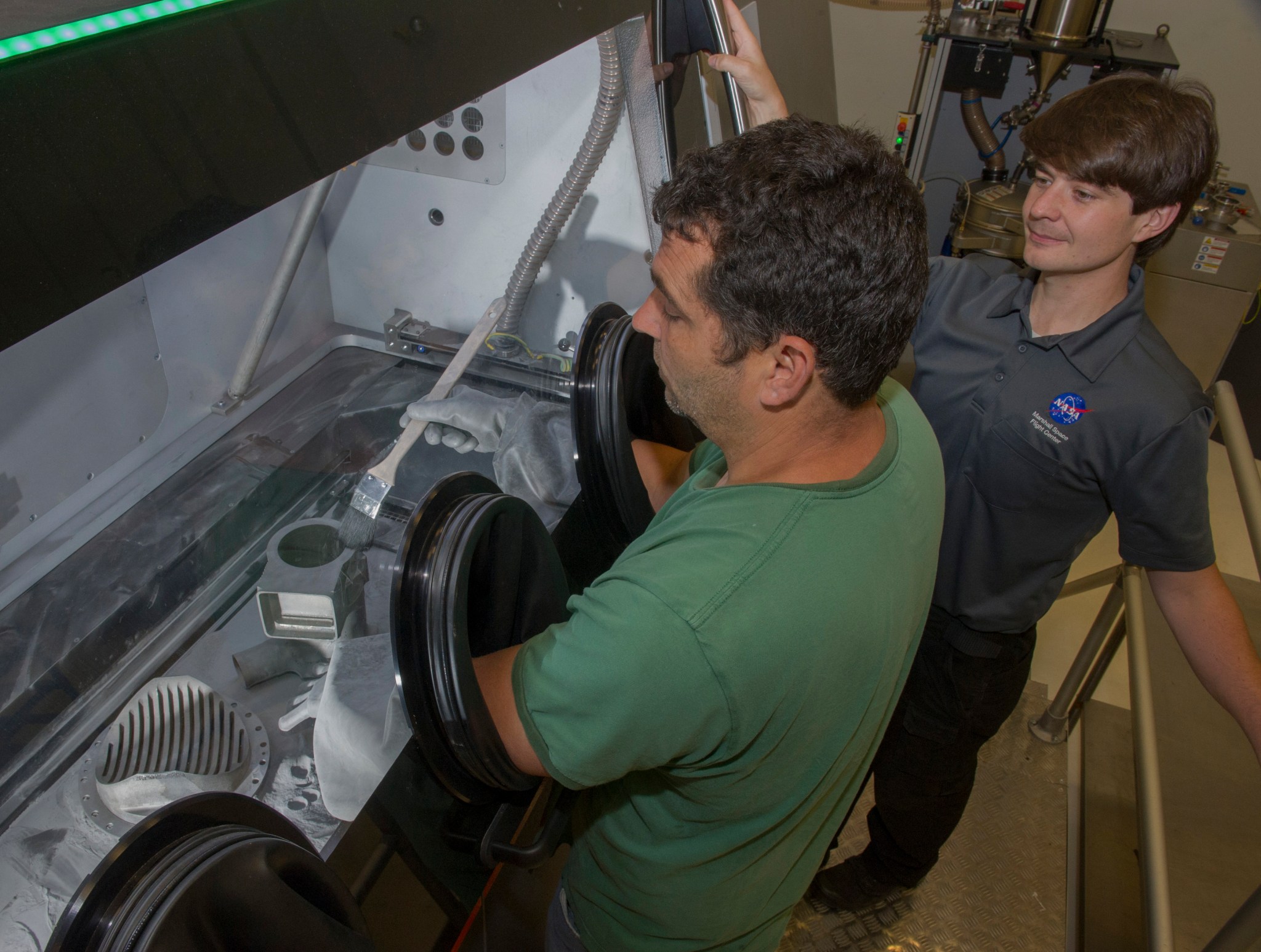 Marshall Center engineers Jim Lydon, left, and Zach Jones work on a recently 3-D printed rocket part. 