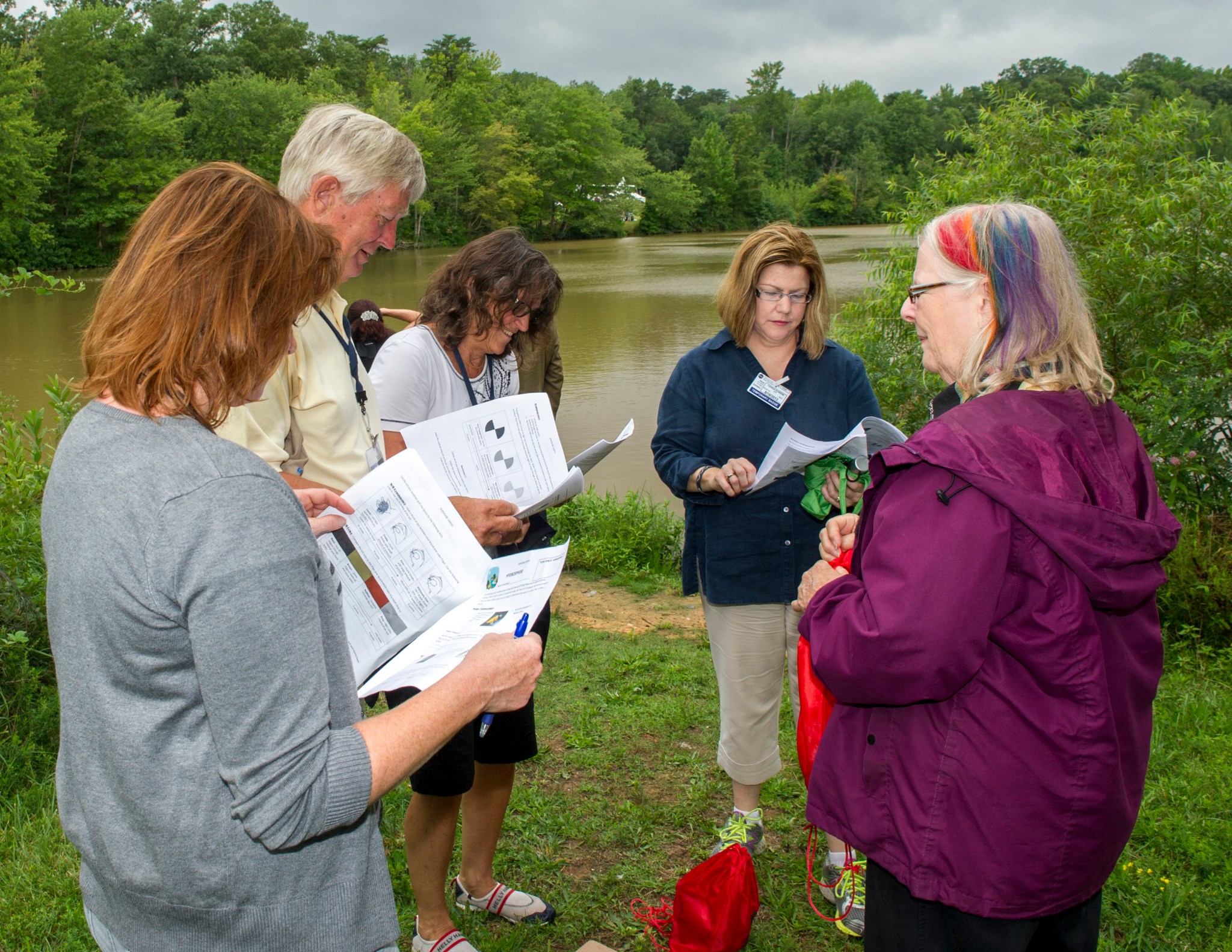 Several teachers read pamphlets in front of a body of water
