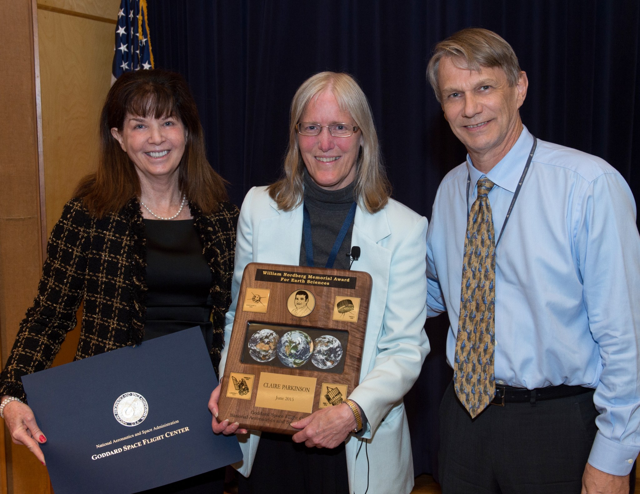 Three people and a plaque, smiling