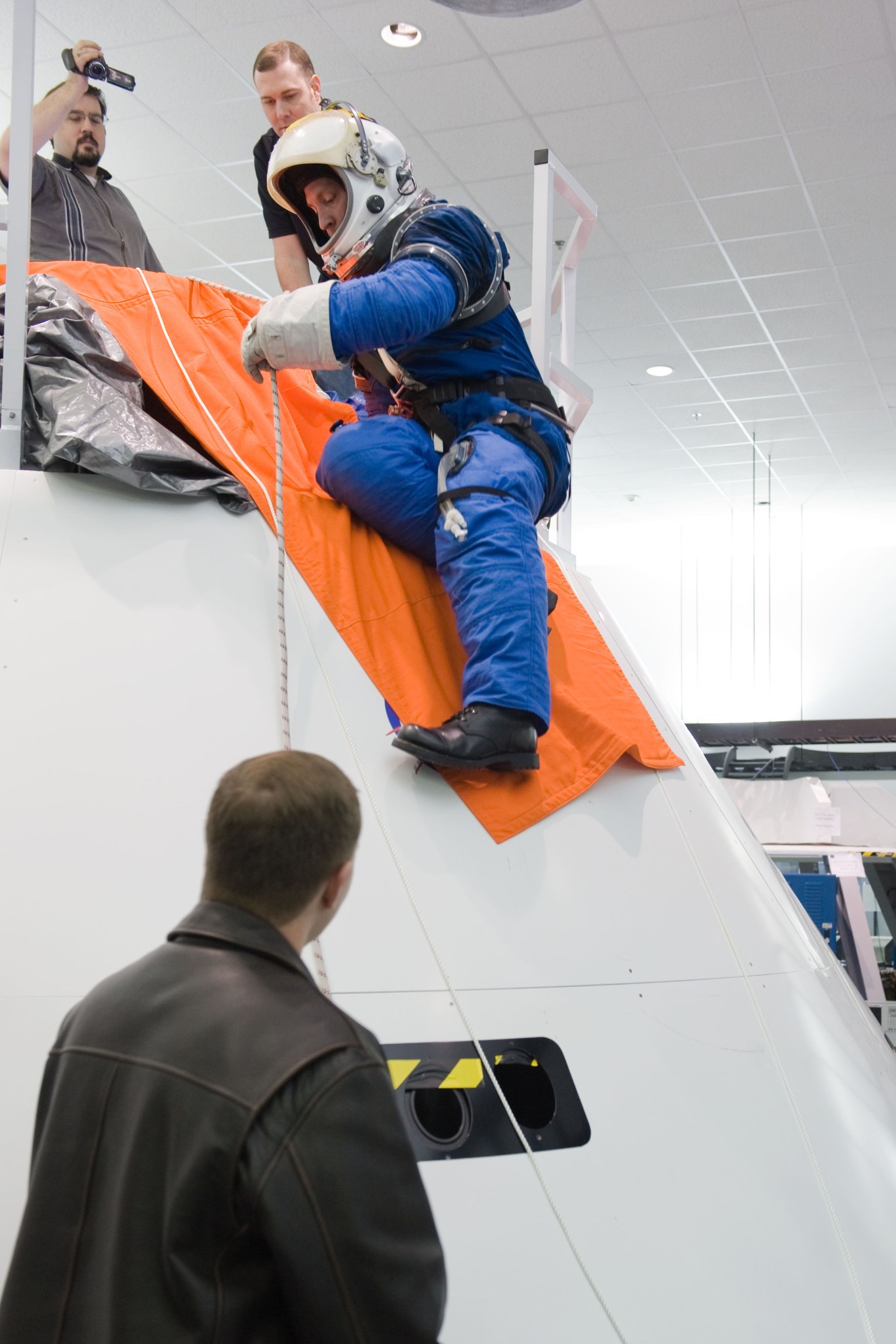 A man practices an emergency escape through the docking port hatch at the top of a model of the Orion spacecraft