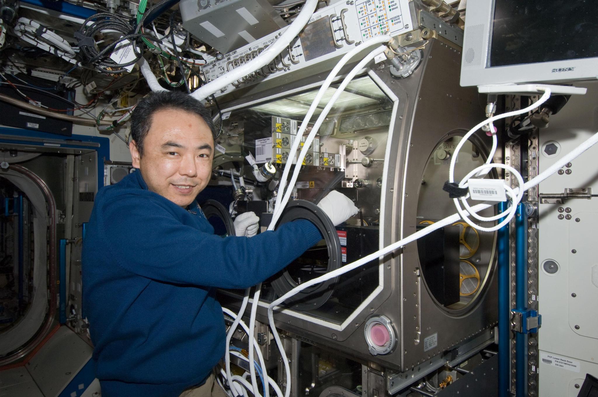 An astronaut works at a glovebox in a space station lab