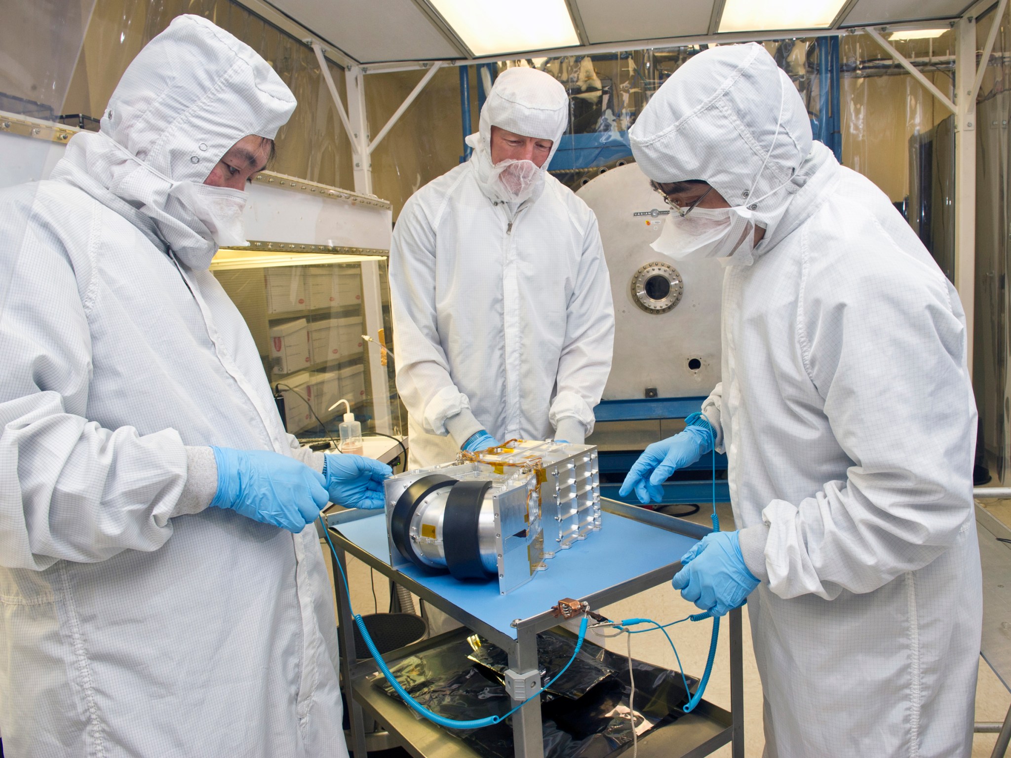 Three engineers dressed in white lab clothes prepare a spectrometer for tests