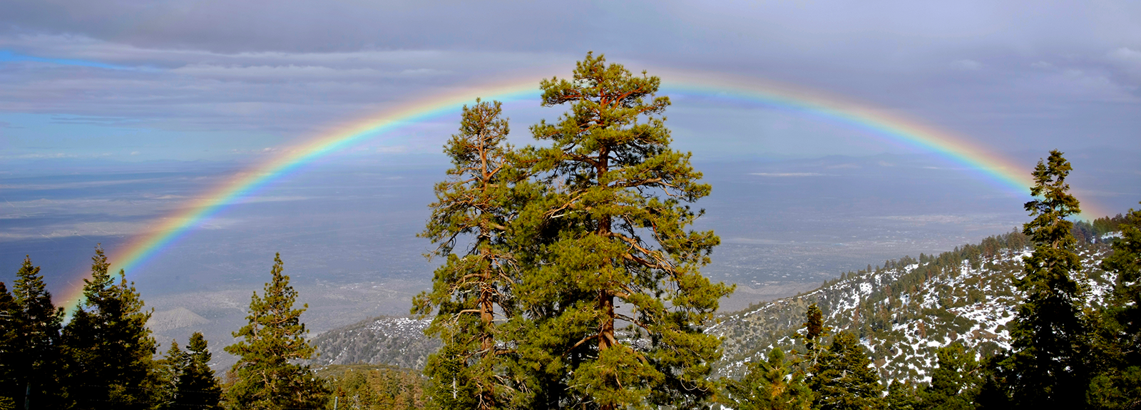 View from a mountaintop of a large rainbow with a valley in the background