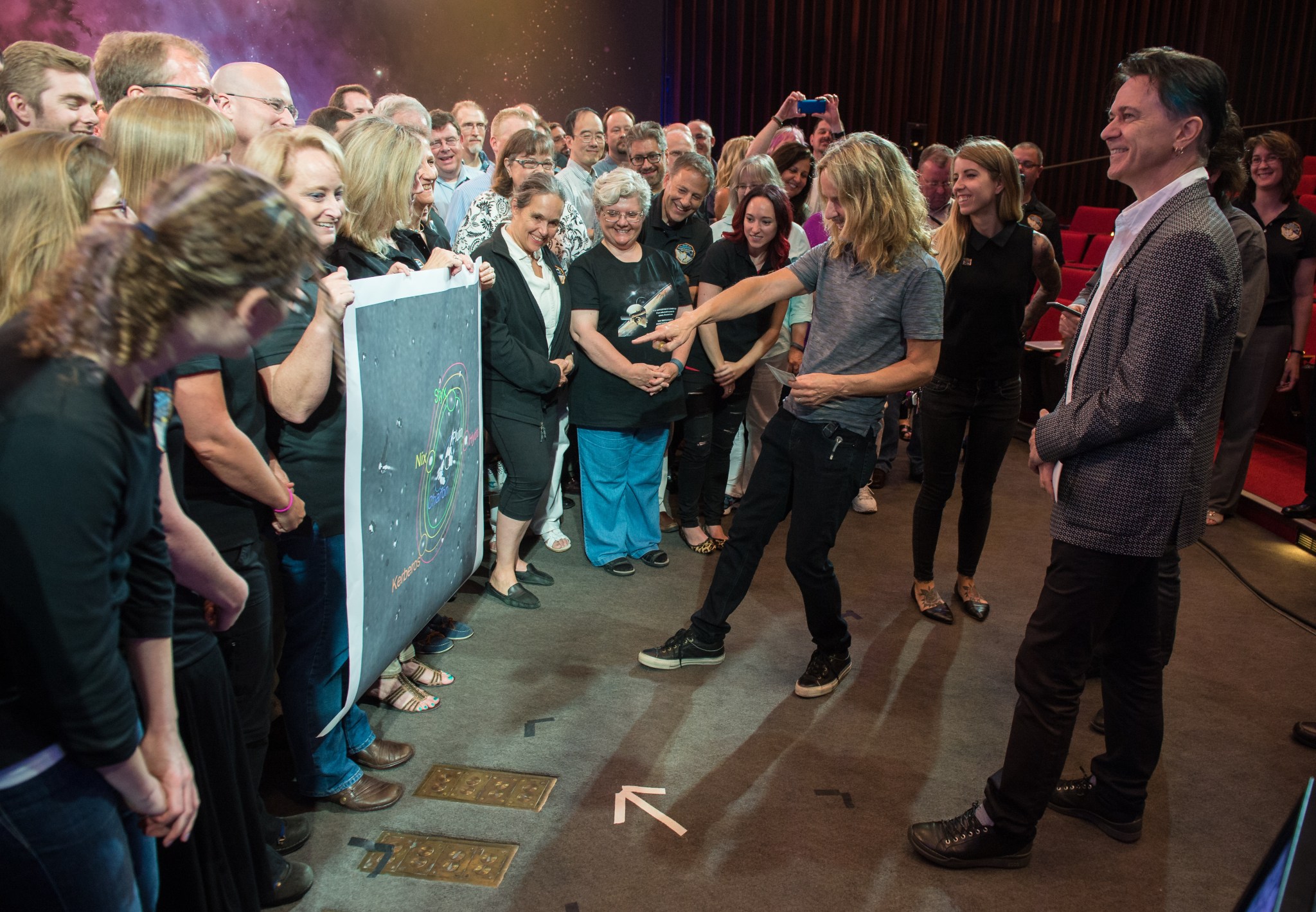 Styx’s Tommy Shaw points out Pluto’s smallest moon with New Horizons team members looking on