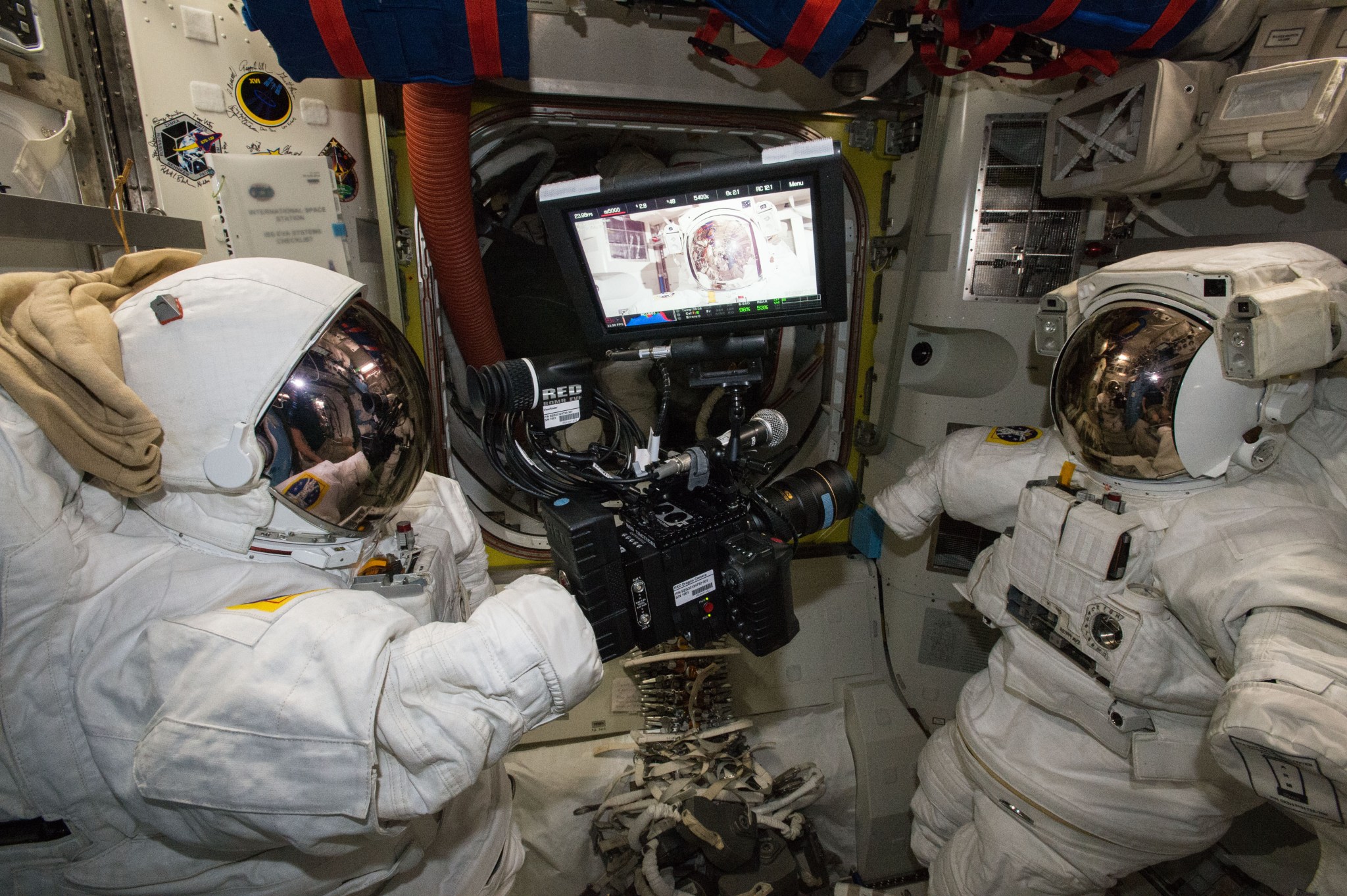 View of RED video camera and display monitor floating between two Extravehicular Mobility Units (EMUs) in the airlock. 