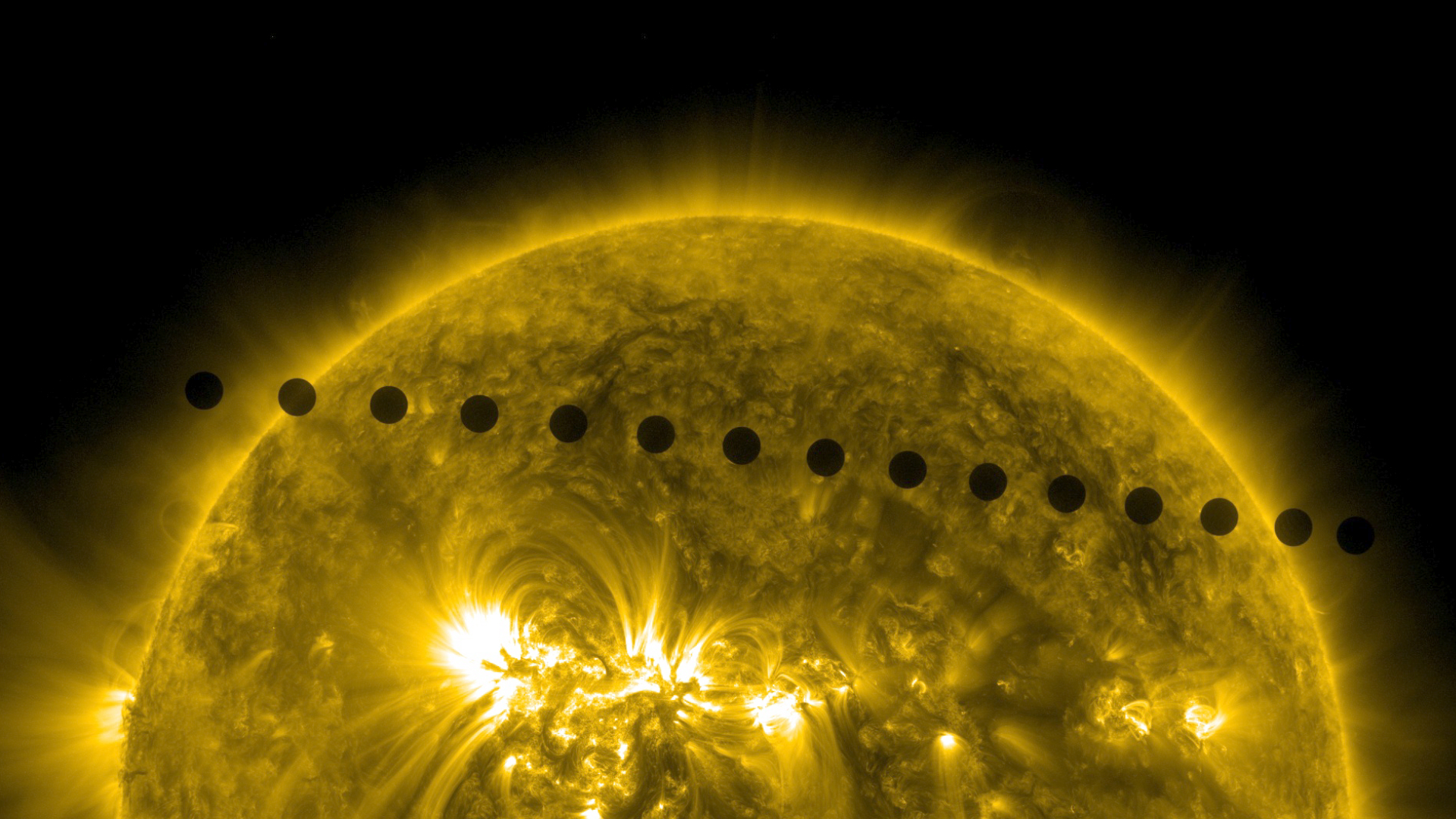 The top half of the Sun appears yellow. About a dozen black circles, all the same size, cross the Sun in a line from left to right.