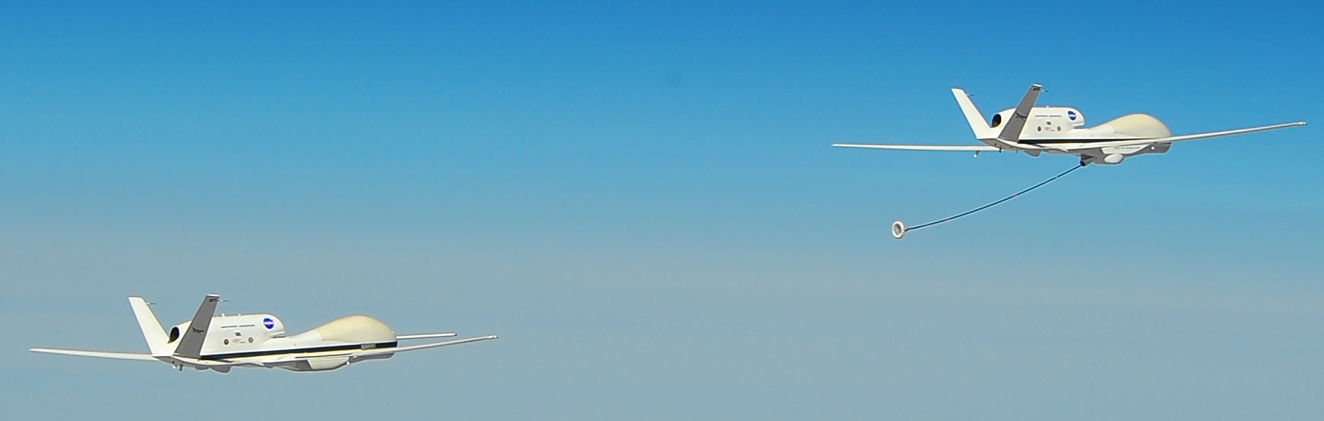 NASA's two Global Hawk unmanned aircraft, one with a refueling hose trailing behind, fly in close formation.