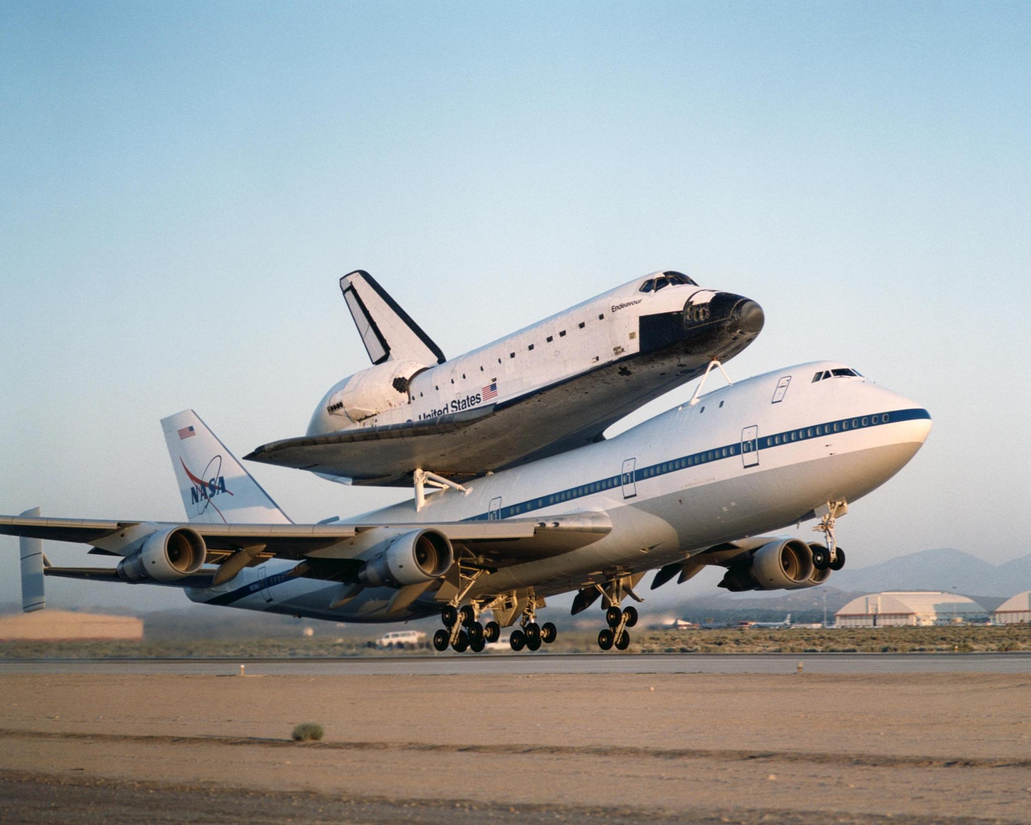A space shuttle orbiter bolted atop its 747 carrier aircraft takes off from a runway in California.