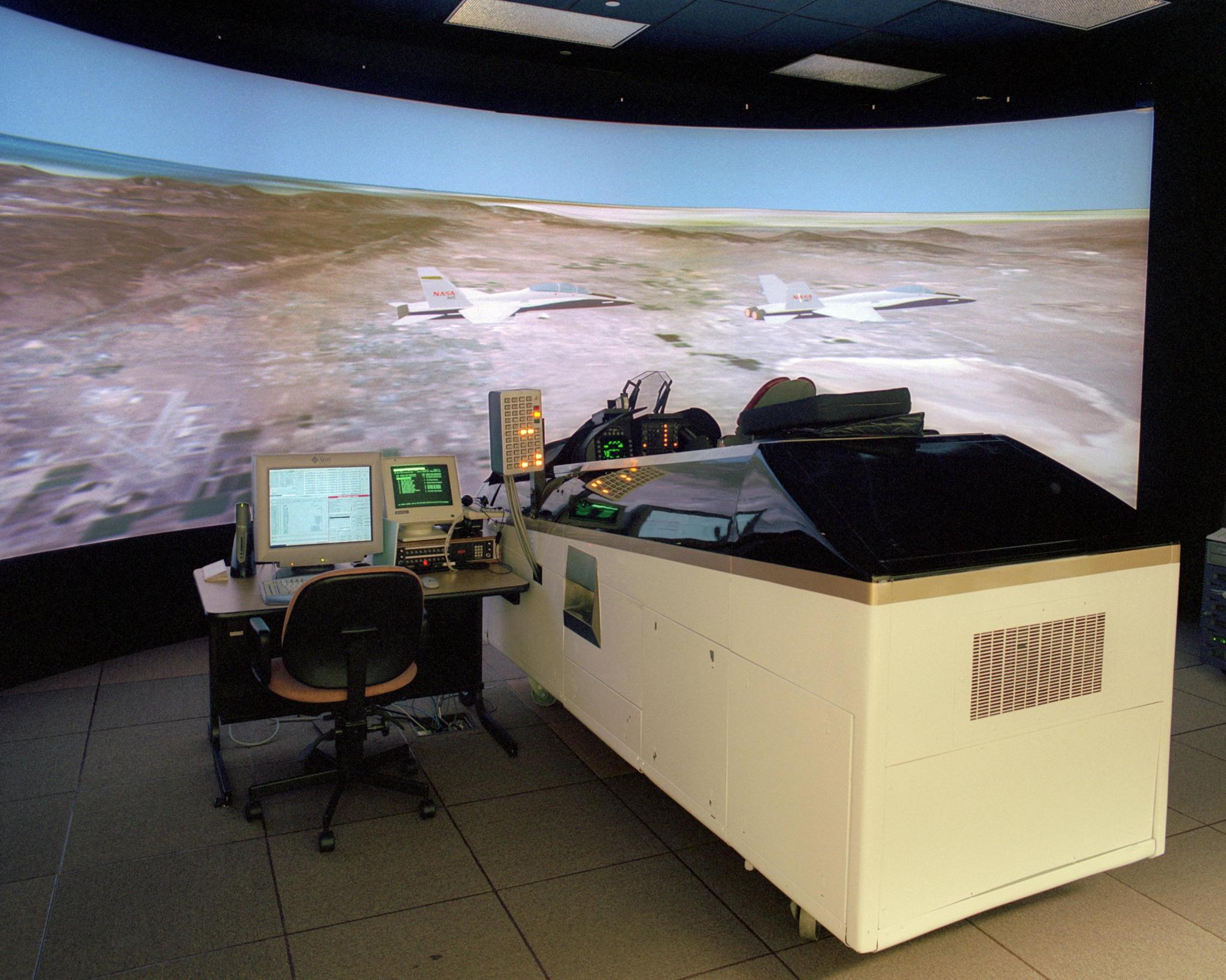 A flight simulator with a large screen showing two plans in flight over land.