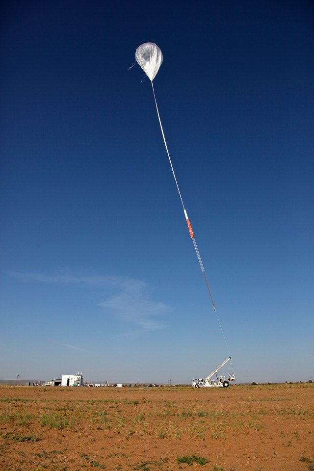 A scientific balloon partially inflated in the sky right before it's released by the crane holding it on the ground.