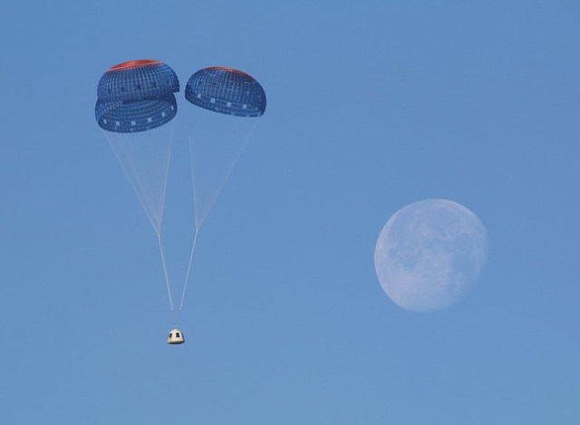 Blue Origin's New Shepard crew capsule under three parachutes in blue sky with Moon in background