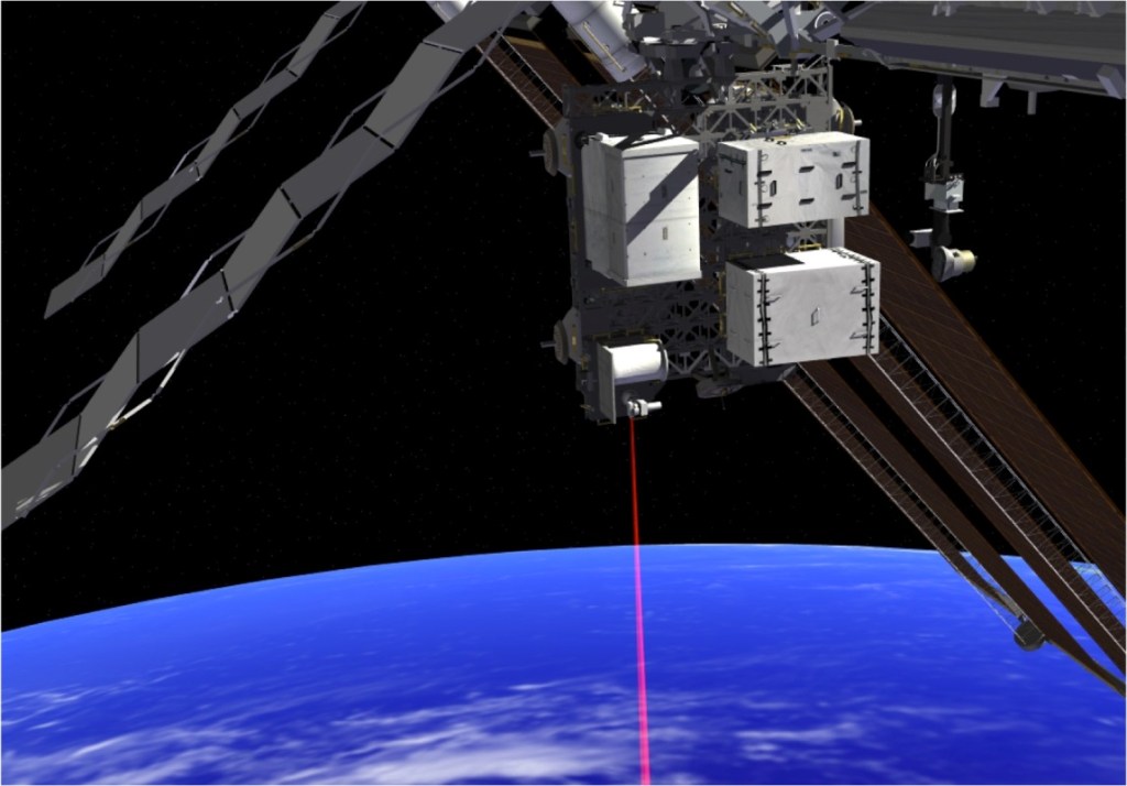A piece of mounted technology against a black sky. The payload is gray, featuring a diamond grating with three visible white components mounted to its surface. A cylindrical apparatus at the bottom emits a red beam downward towards the blue curve of the Earth's surface. Components of the International Space Station are visible in the background.