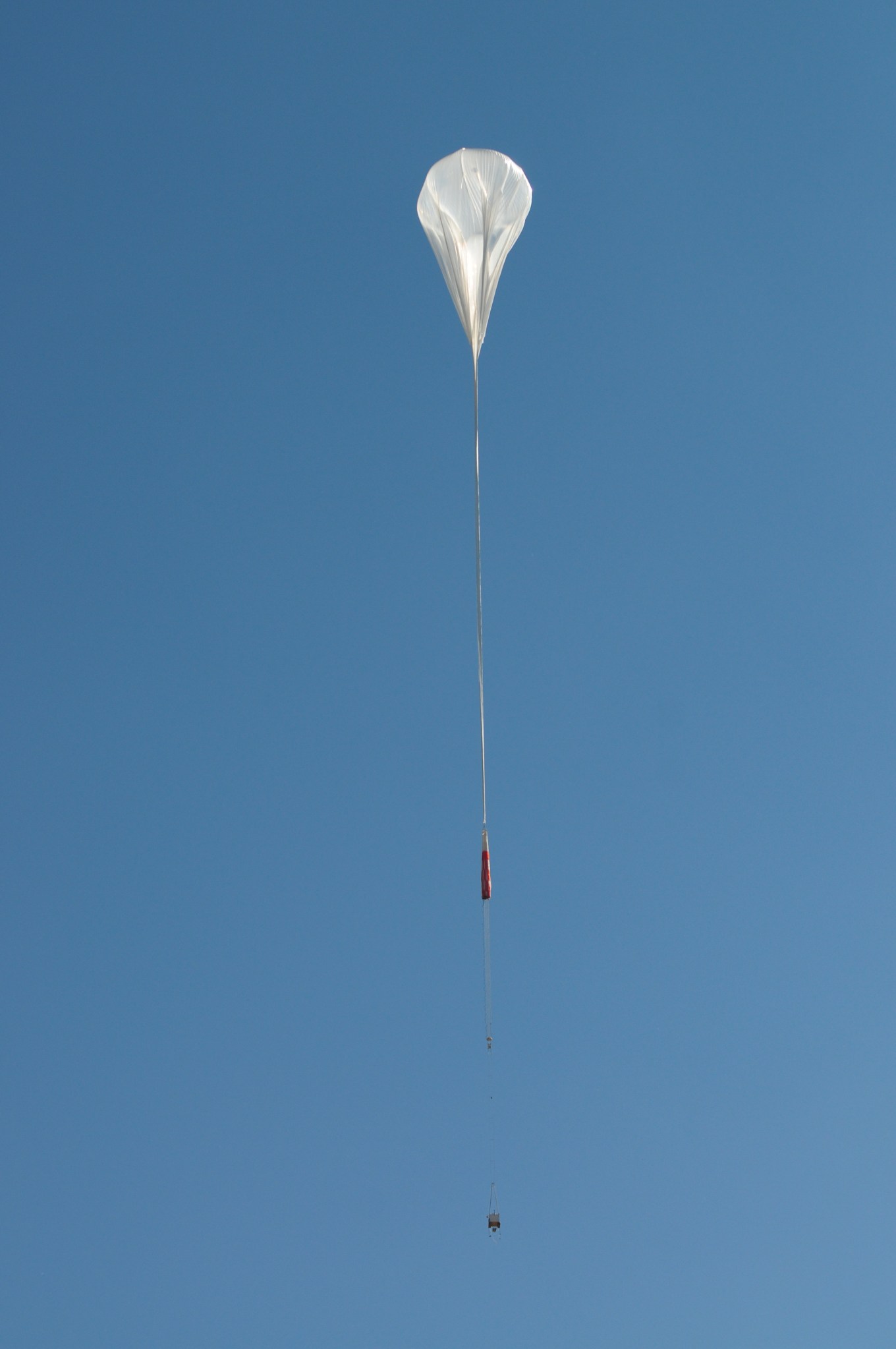 A partially inflated balloon just after liftoff in the sky.