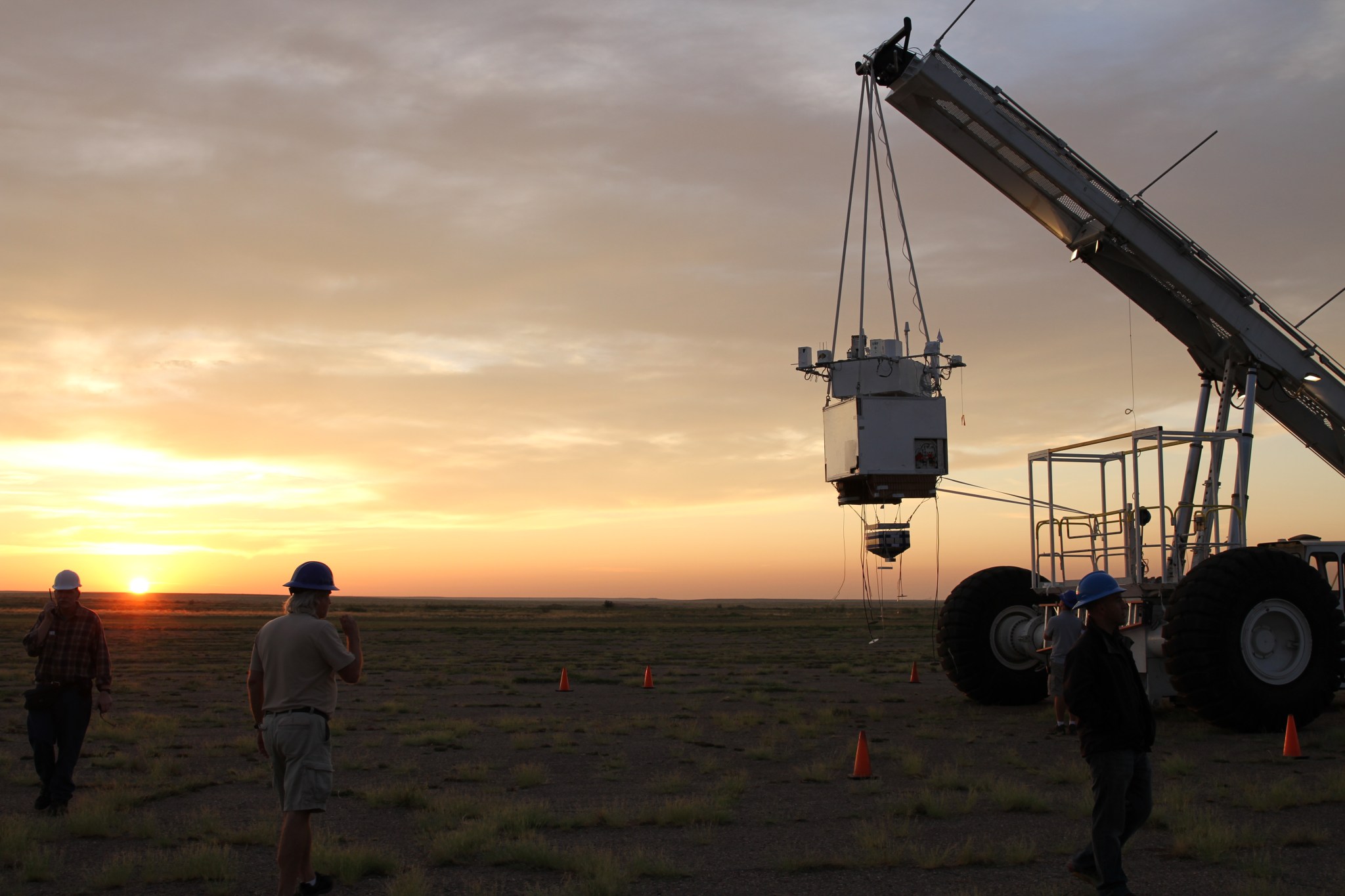 The HASP student payload hangs from a crane, the sun rising in the background.