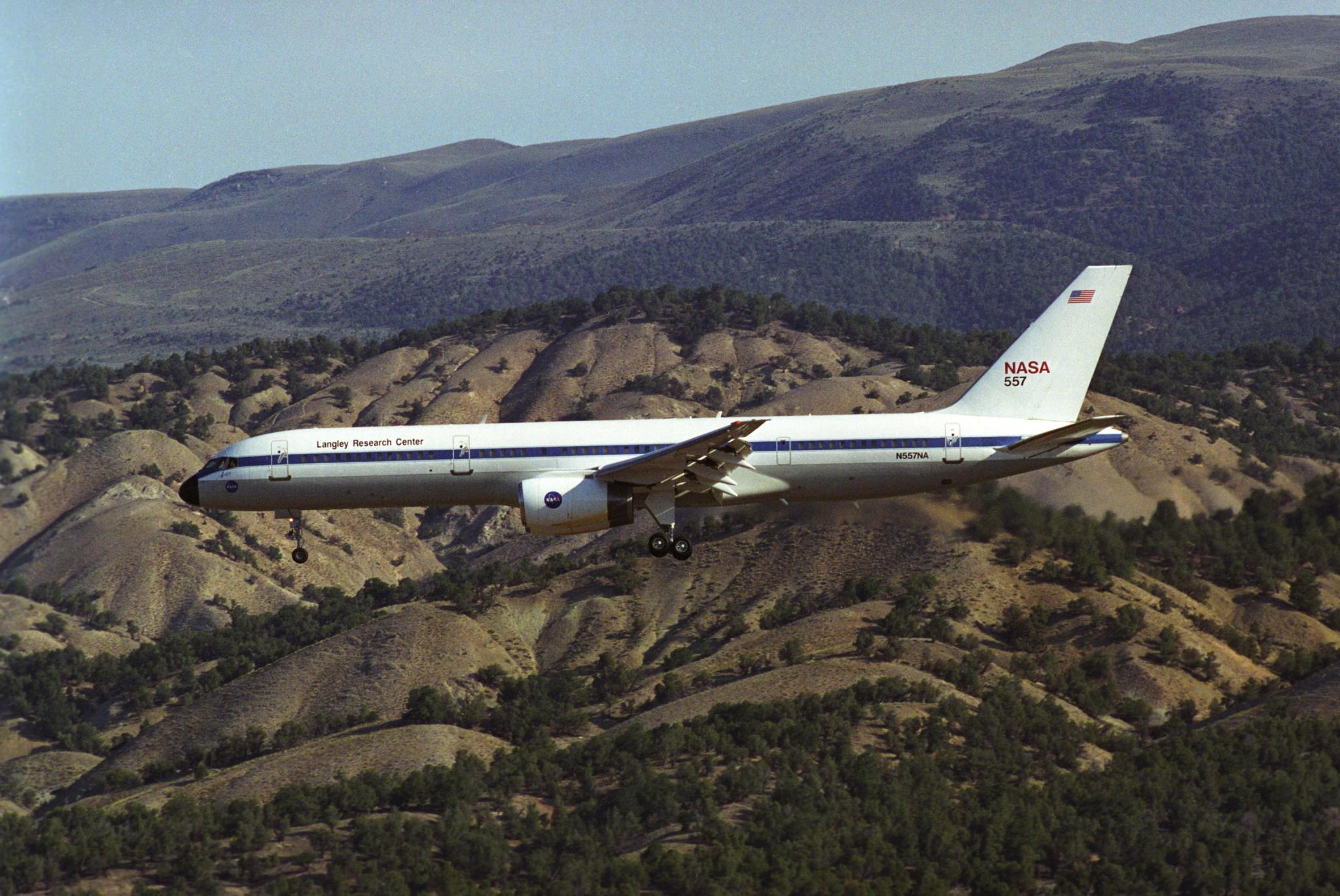 A picture of an airplane flying over some hills.