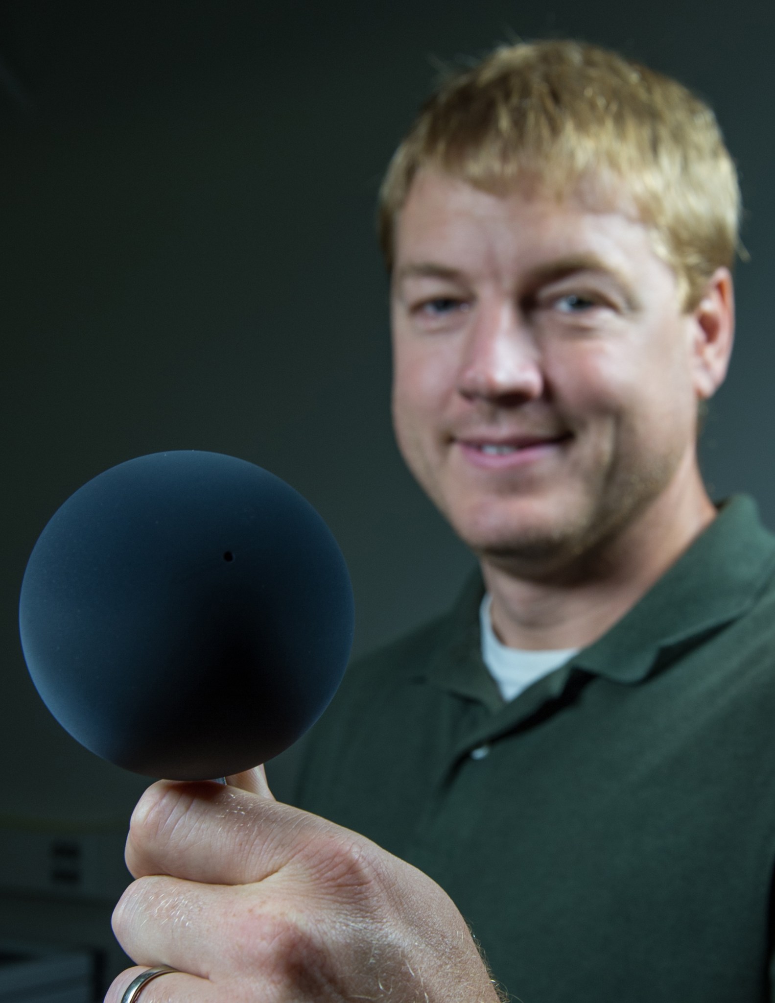 Phillip Chamberlin smiles at the camera while holding a grapefruit-sized black sphere coated in carbon nanotubes. 
