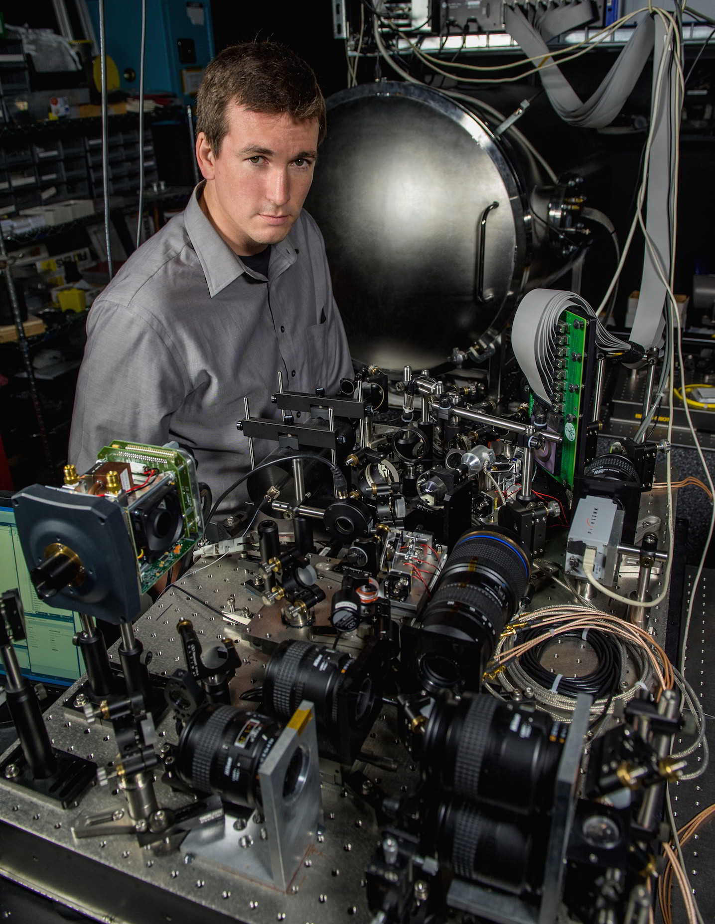 Man with fair skin and brown hair wearing a grey button down stands next to the latest incarnation of the Visible Nulling Coronagraph.