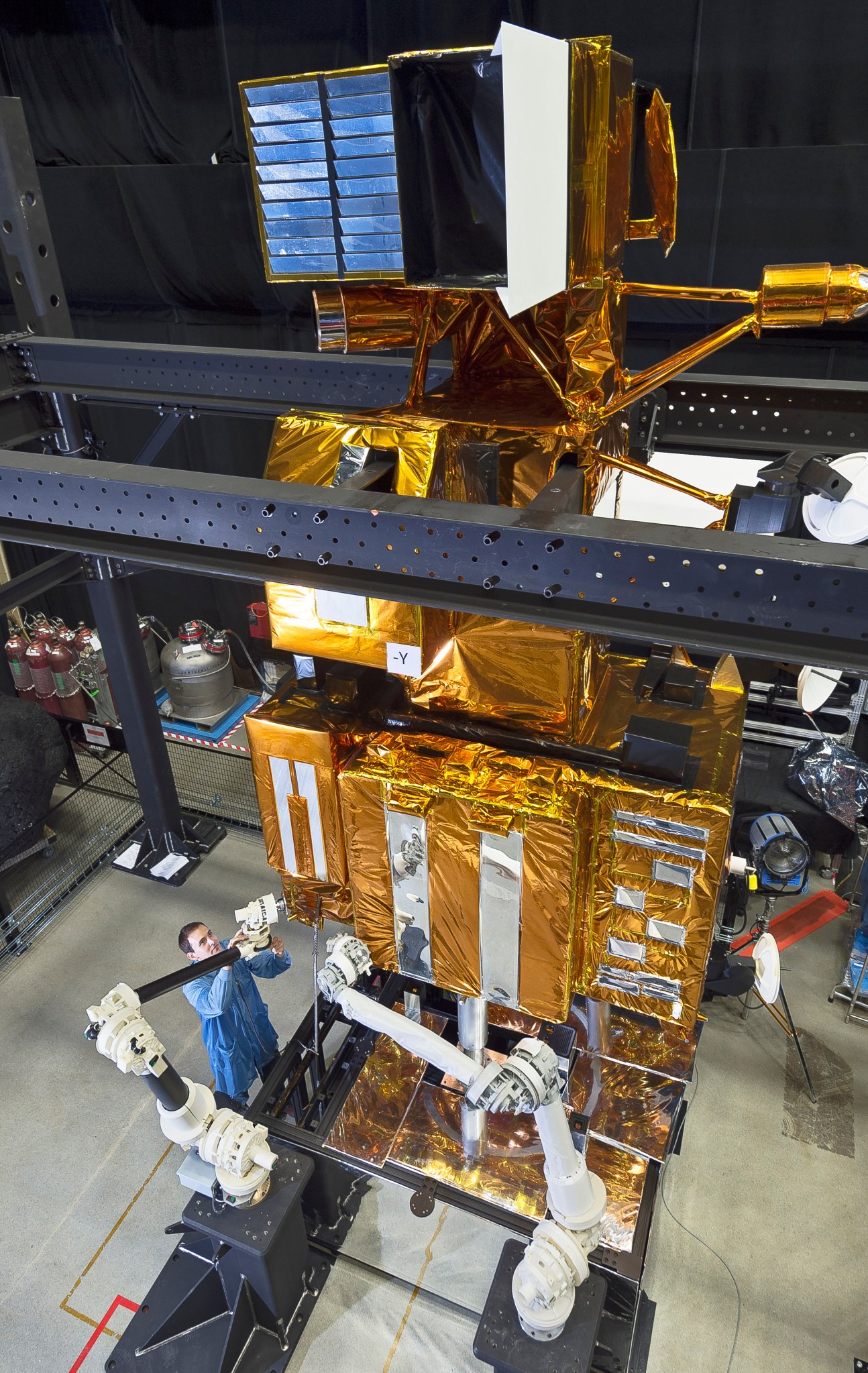 Engineer wearing a blue lab coat drills equipment onto a very large Landsat mockup