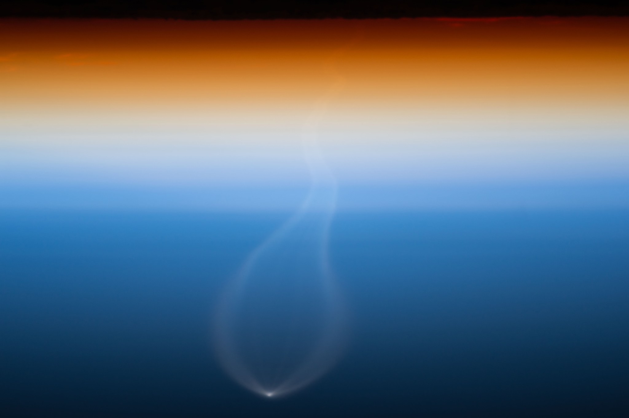 Earth's atmosphere at sunset with bright spot of rocket launch visible below