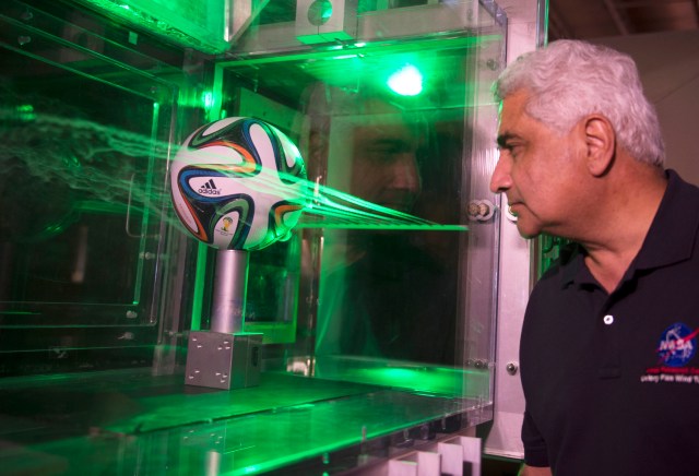 man looking at soccer ball in a water chamber with lasers around it