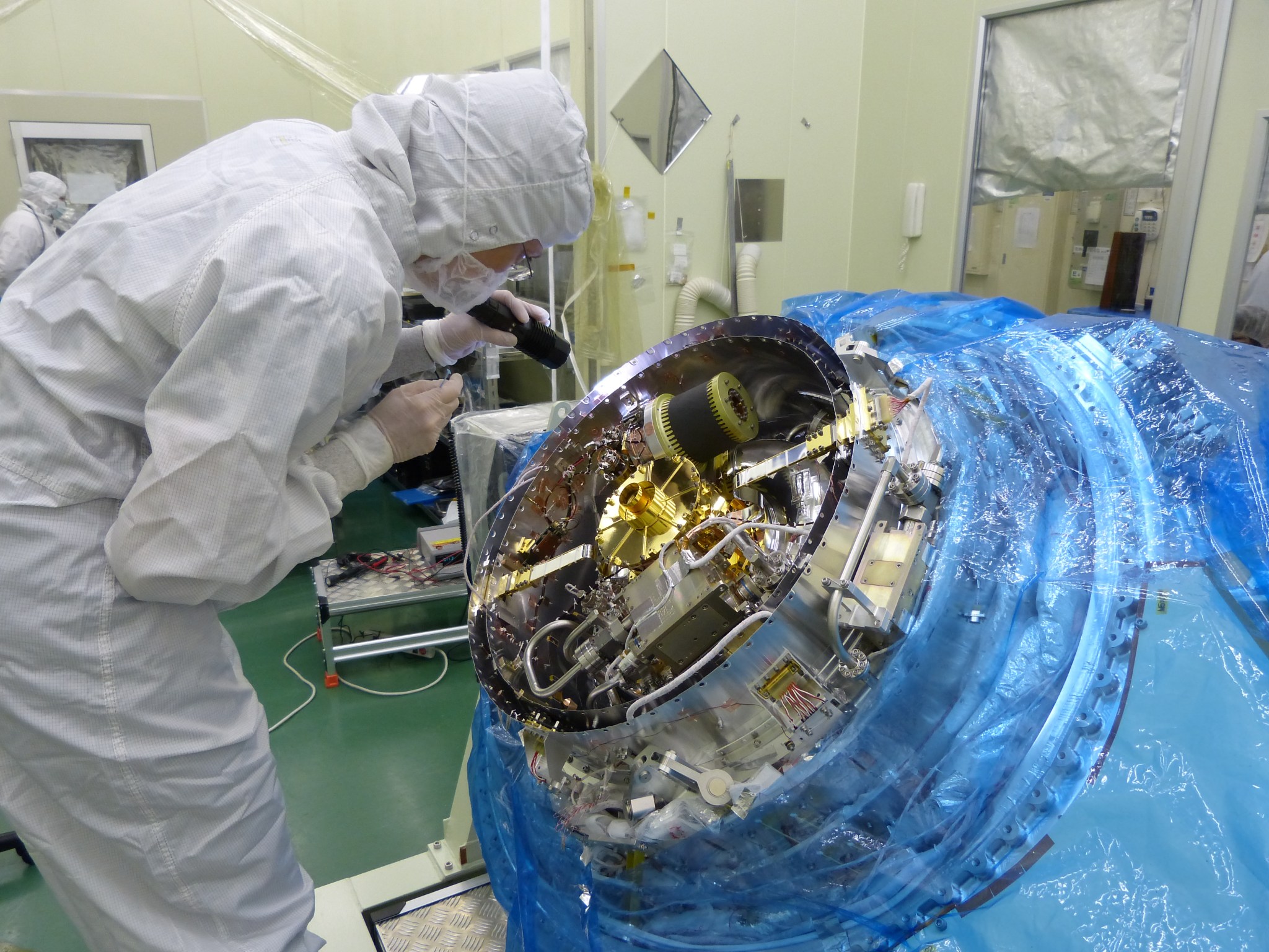 Person in clean room gear inspecting Hitomi before its final closing.