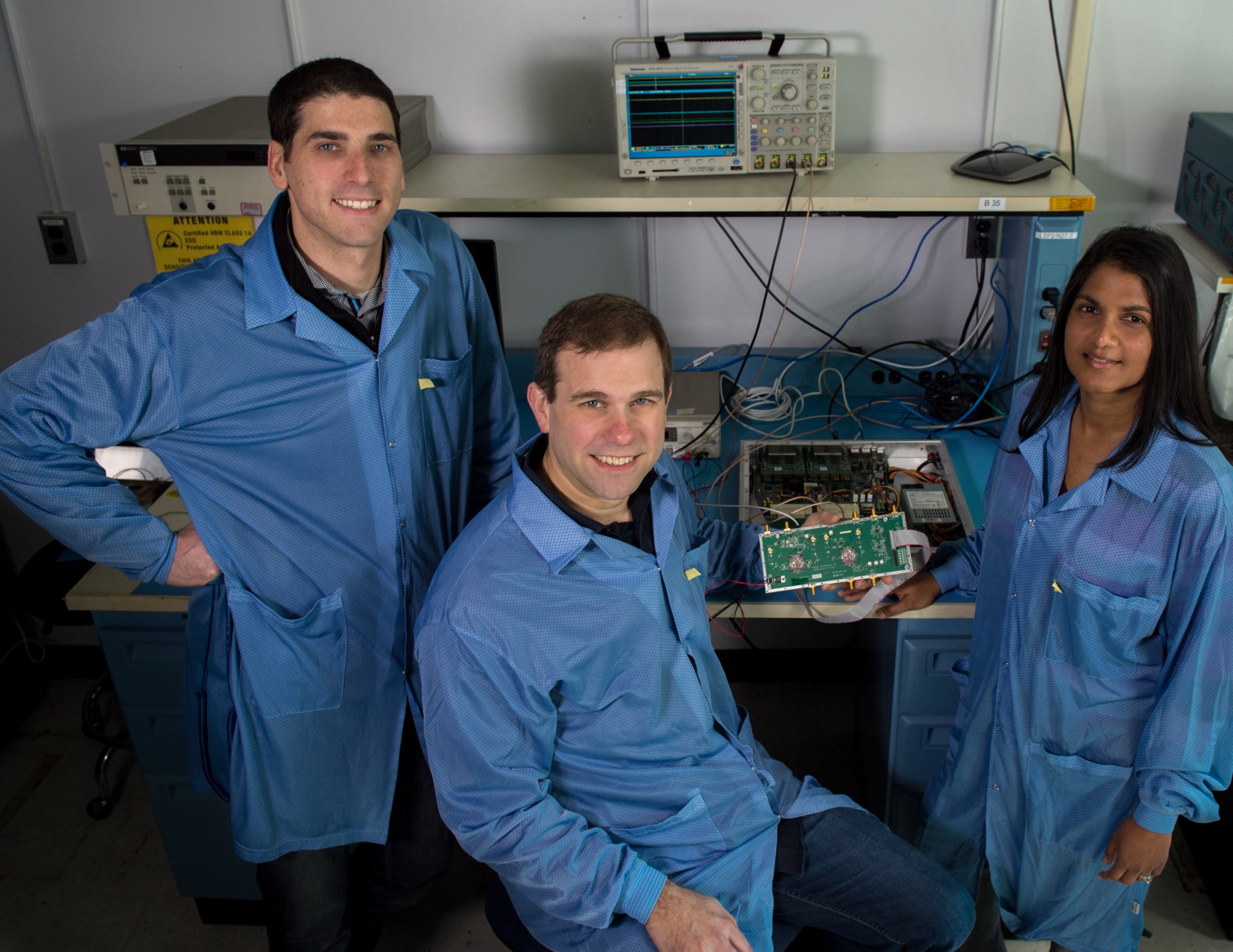 three people in blue paper suits pose with tech