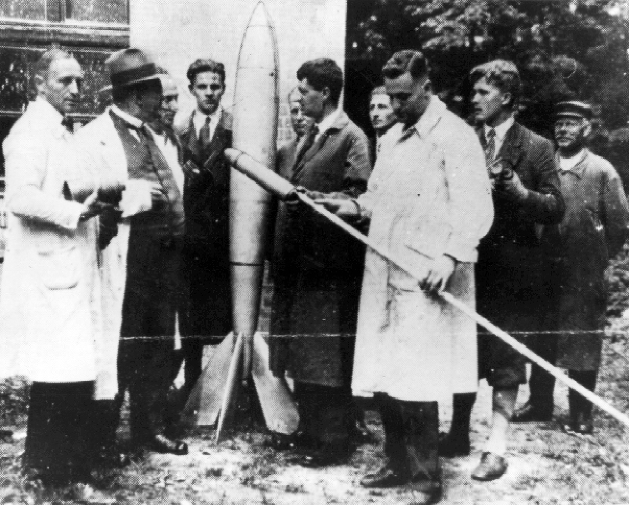 Group of rocket experimenters standing next to a rocket. One of them holds a rocket attached to a long pole.