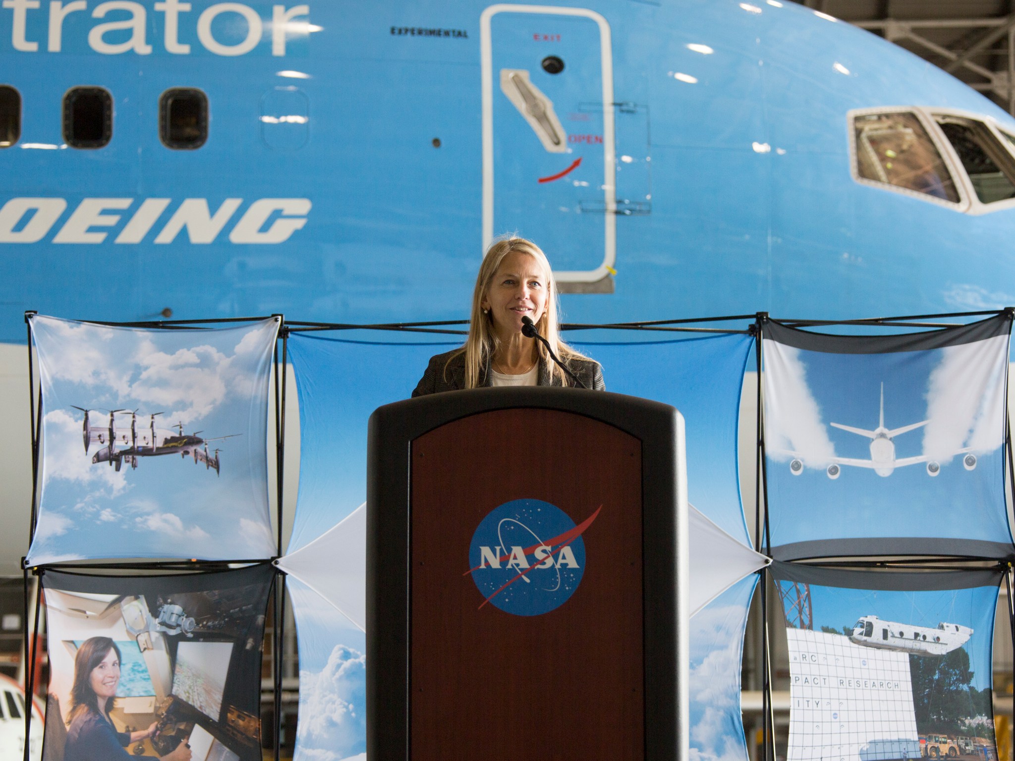 NASA Deputy Administrator Dava Newman stands at a podium in front of the Boeing ecoDemonstrator 757, parked at NASA Langley.