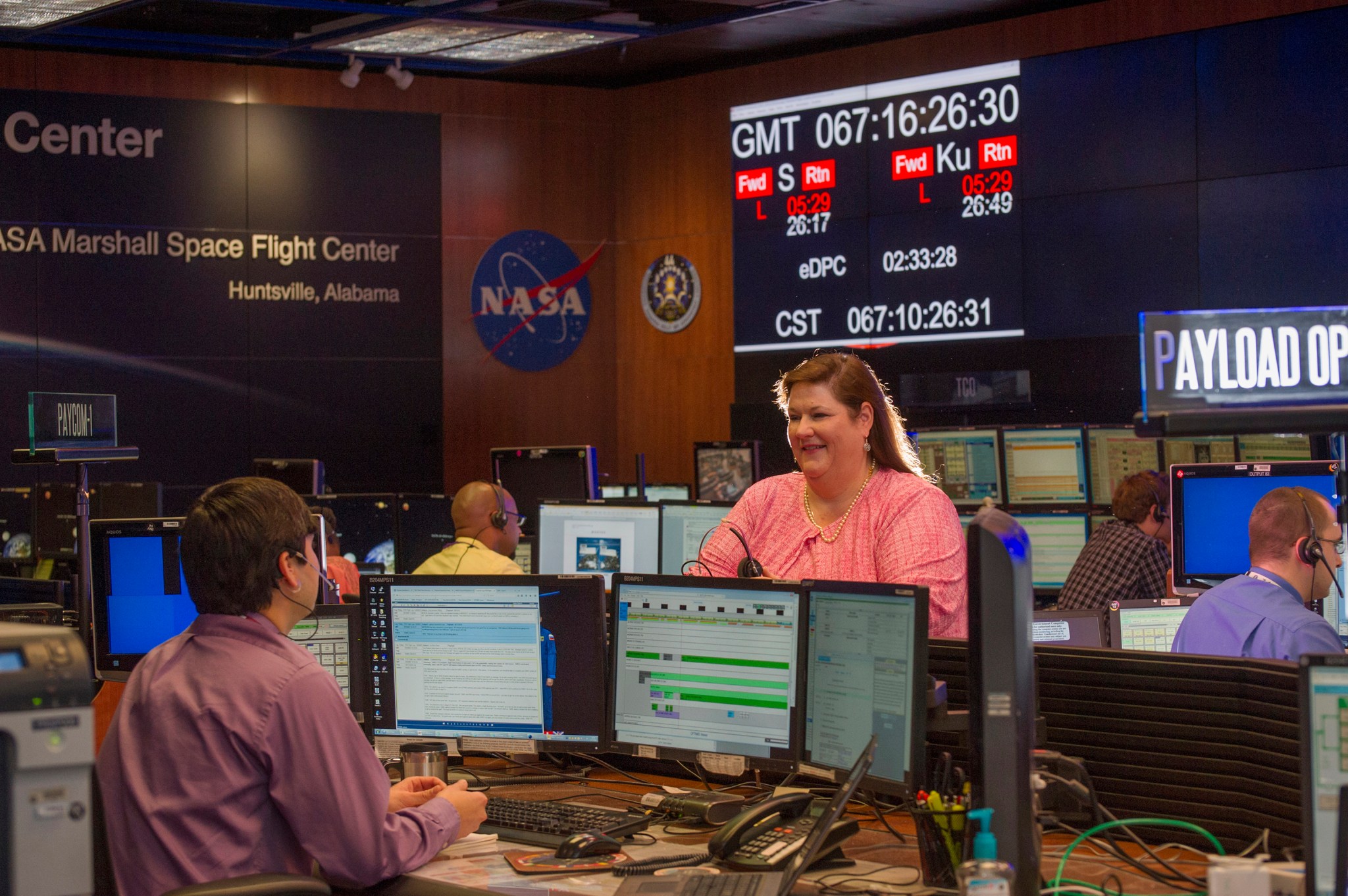 Pat Patterson, standing at center, lends advice to Daniel Shafer, left, a payload operations director-in-training.